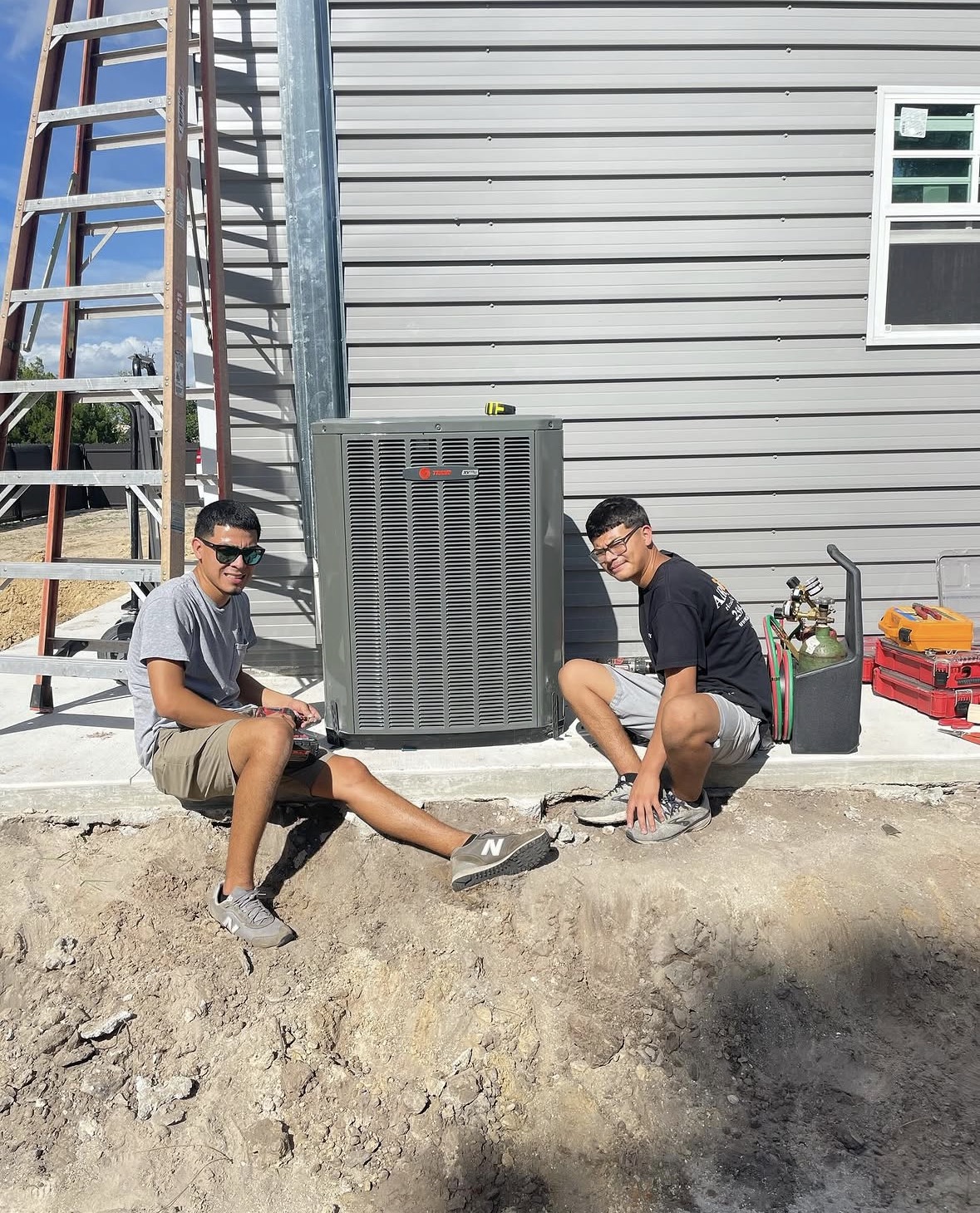 Daniel Jr. and Cristian on a jobsite next to a newly-installed Trane condenser